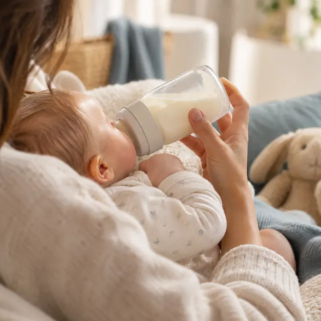 Bébé qui boit son biberon dans les bras de son parent